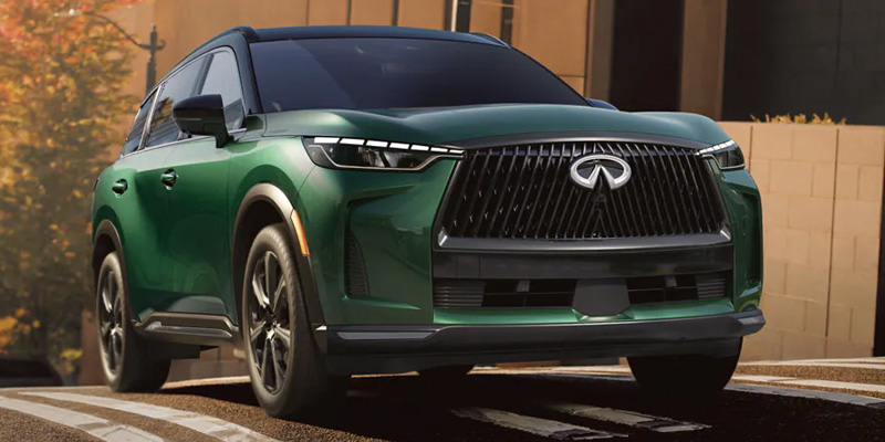 A green luxury QX60 with a sleek design, dynamic grille, and sharp headlights is parked in an urban setting, conveying elegance and power.