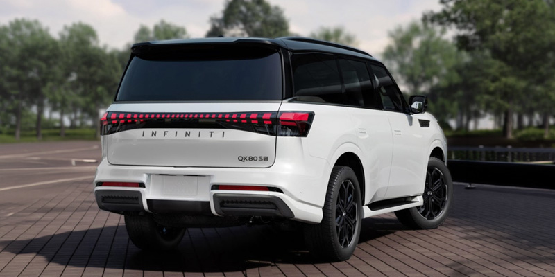 Rear view of a white Infiniti QX80 SUV parked on a brick road. The vehicle features sleek, modern design elements and stands amidst a lush, green, tree-lined background.
