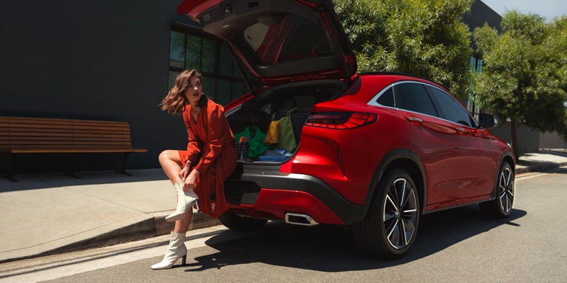 girl leaning on the back of a red INFINITI XQ55 with trunk hatch open